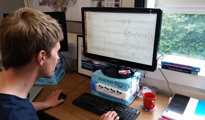 A photo of a volcanic seismologist looking at seismograms on a computer screen, selecting Icelandic earthquakes for further analysis.