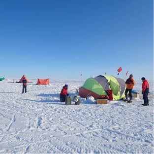Photo showing scientists working in Antarctica with base camp behind