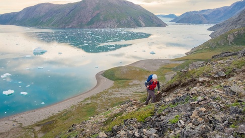 Photo showing mountains and a river with a person climbing the hill