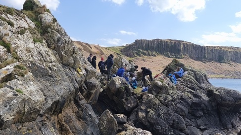 Photo of students sat on an outcrop with the Doon sill in the background