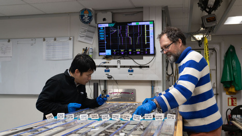 Photo of two men examining cores of rock laid out on a table.