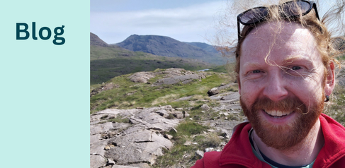 Selfie of a man in the field, with bare rock outcrops and mountains in the background