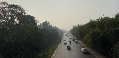 Image of a busy road in Lahore, surrounded on either side by trees and with a smoggy sky blocking out the sun