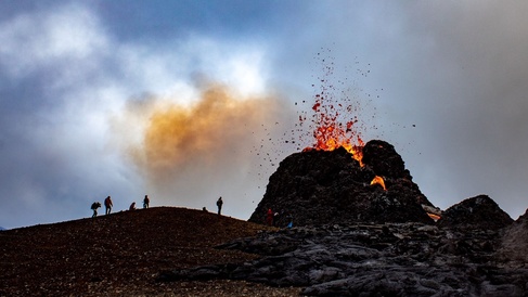 Photo showing a volcanic spatter cone erupting with lava coming out of the top
