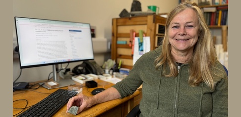 A photo of a woman sat at her computer desk holding a green rock