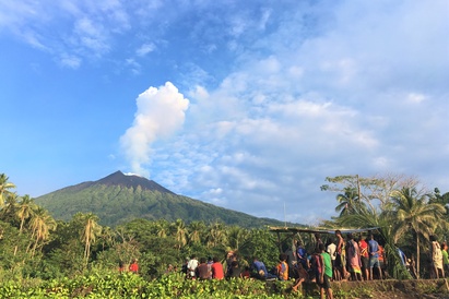 Manam islanders gathering together in the shadow of the volcano, which is showing a white gas plume against the bright blue sky; image credit Emma Liu, UCL