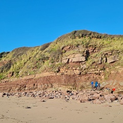 Photo of a sunny beach with three people work close to the red cliff face