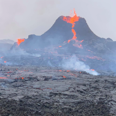 Image of a volcano spewing molton lava, surrounded by a grey lunar landscape and smoke