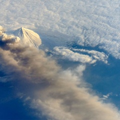 Satellite image of a volcano from space, shrouded in clouds and spewing volcanic ash