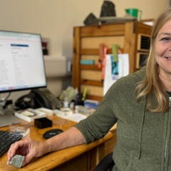 A photo of a woman sat at her computer desk holding a green rock