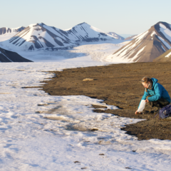 Photo showing a woman knelt down at the edge of some ice taking a sample