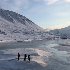 Photo of three people standing in front of a glacier, there are snowy mountains behind