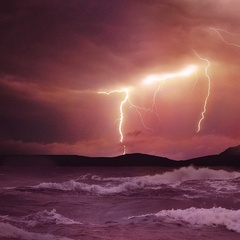 Photo of volcanic eruption with lightning and stormy sea in foreground