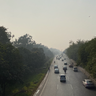 Image of a busy road in Lahore, surrounded on either side by trees and with a smoggy sky blocking out the sun