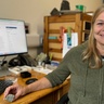 A photo of a woman sat at her computer desk holding a green rock