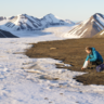 Photo showing a woman knelt down at the edge of some ice taking a sample