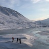 Photo of three people standing in front of a glacier, there are snowy mountains behind