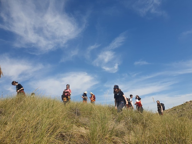 Photo showing a group of students walking in grass with blue sky behind