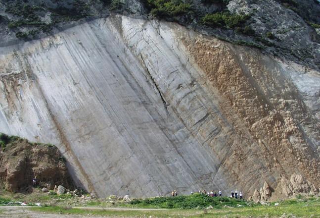 Students looking at a fault scarp. A giant fault scarp with some students at the very bottom for scale