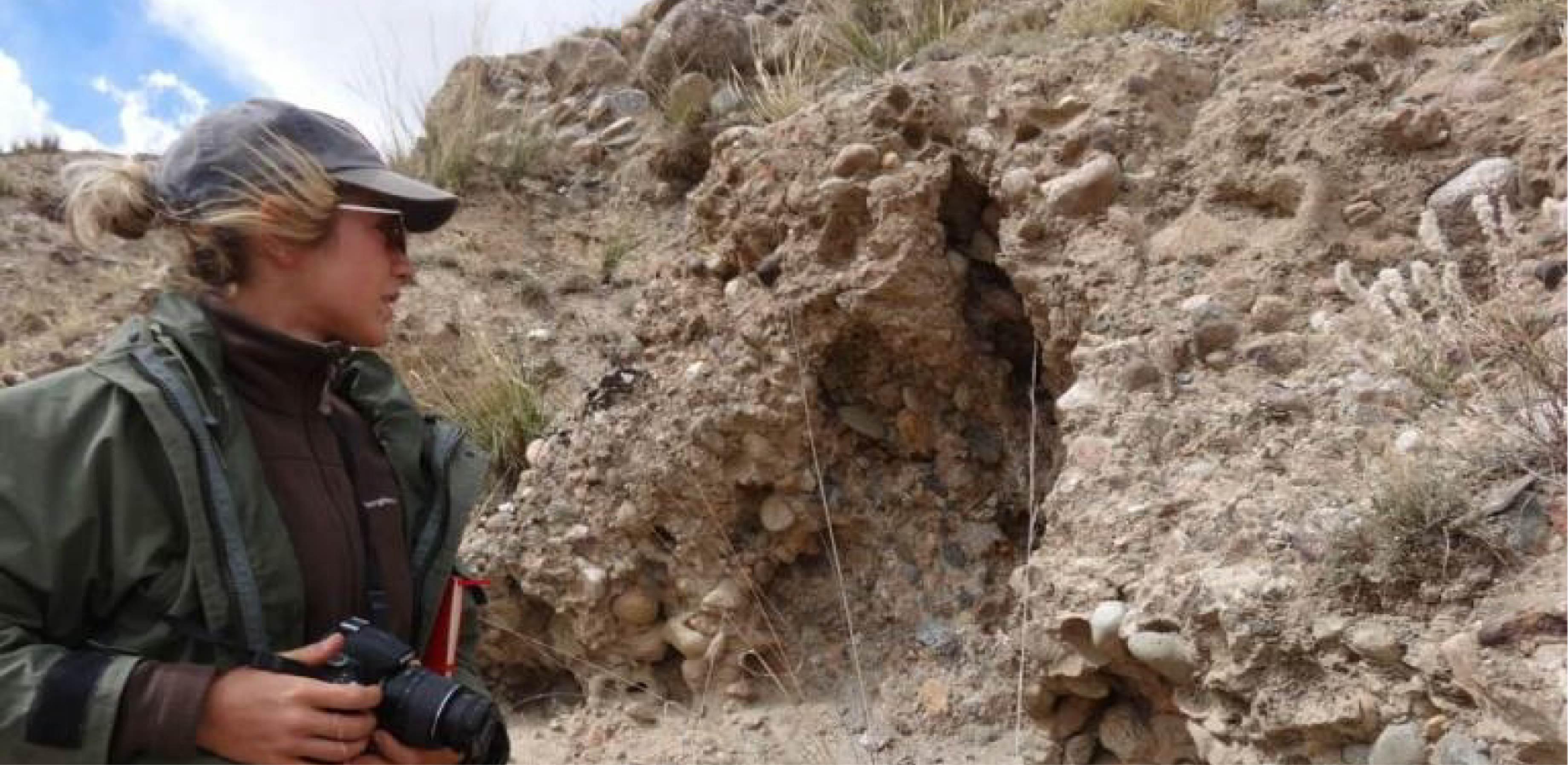Grace standing next to a rock outcrop with a camera