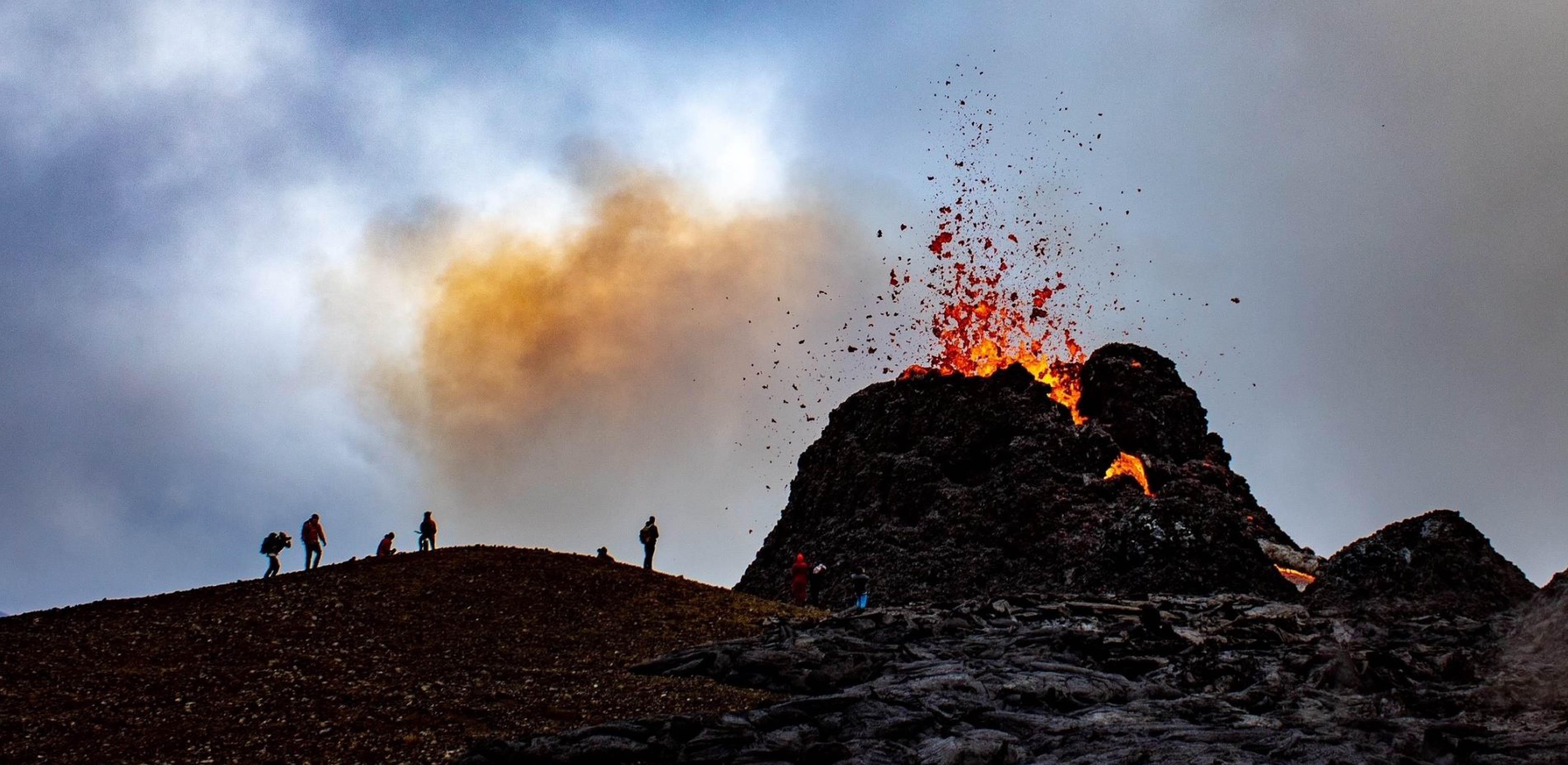 Photo showing a volcanic spatter cone erupting with lava coming out of the top