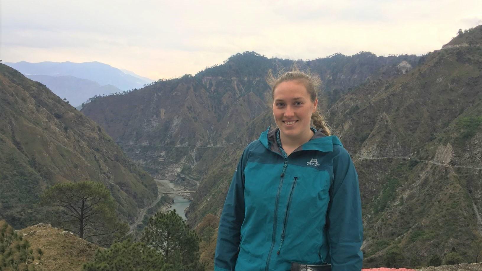 Photo of Aisling on field work, standing in front of mountains, in December 2019