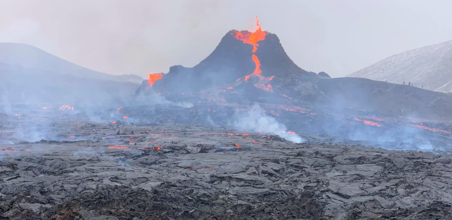 Image of a volcano spewing molton lava, surrounded by a grey lunar landscape and smoke