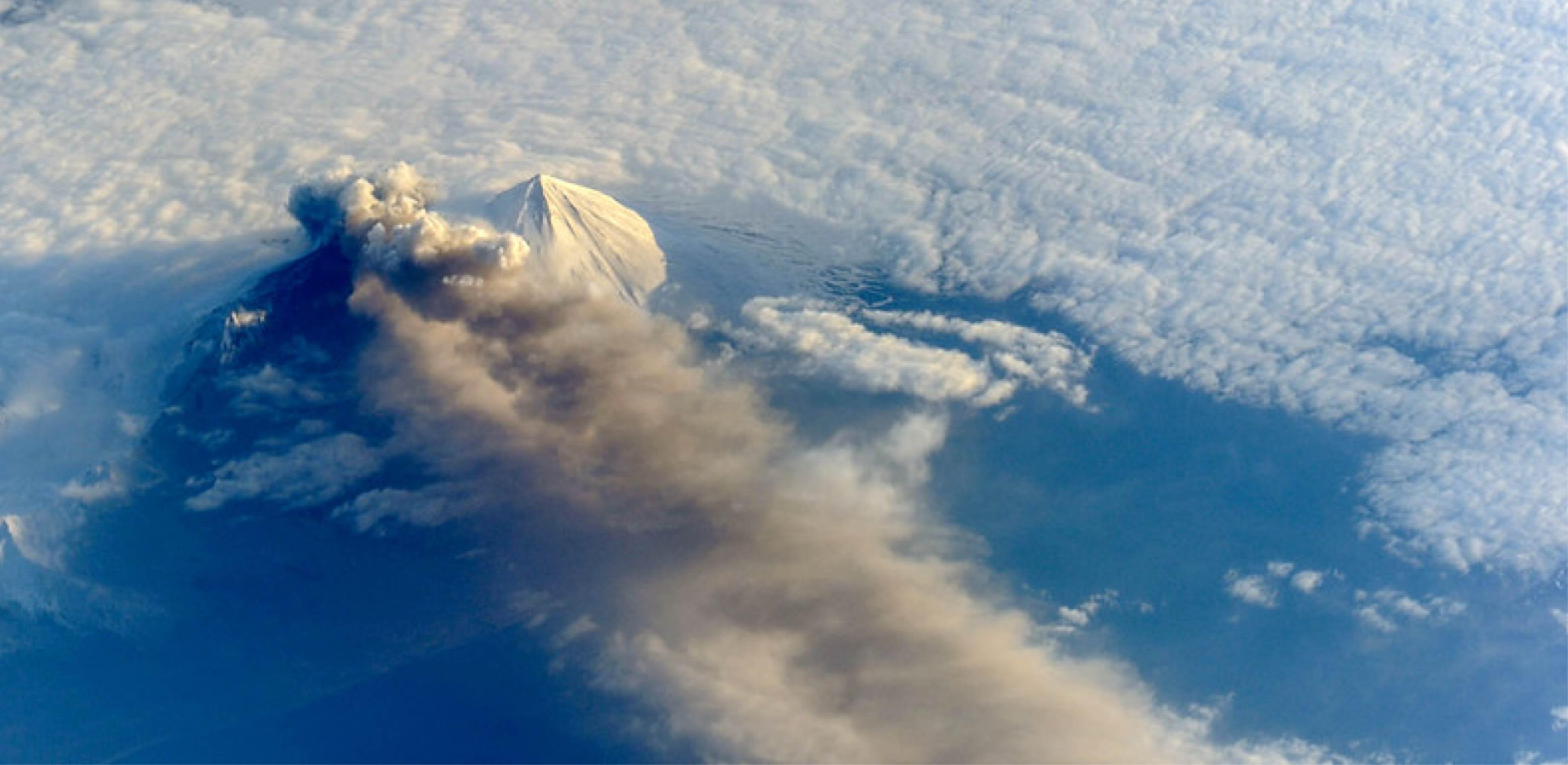 Satellite image of a volcano from space, shrouded in clouds and spewing volcanic ash