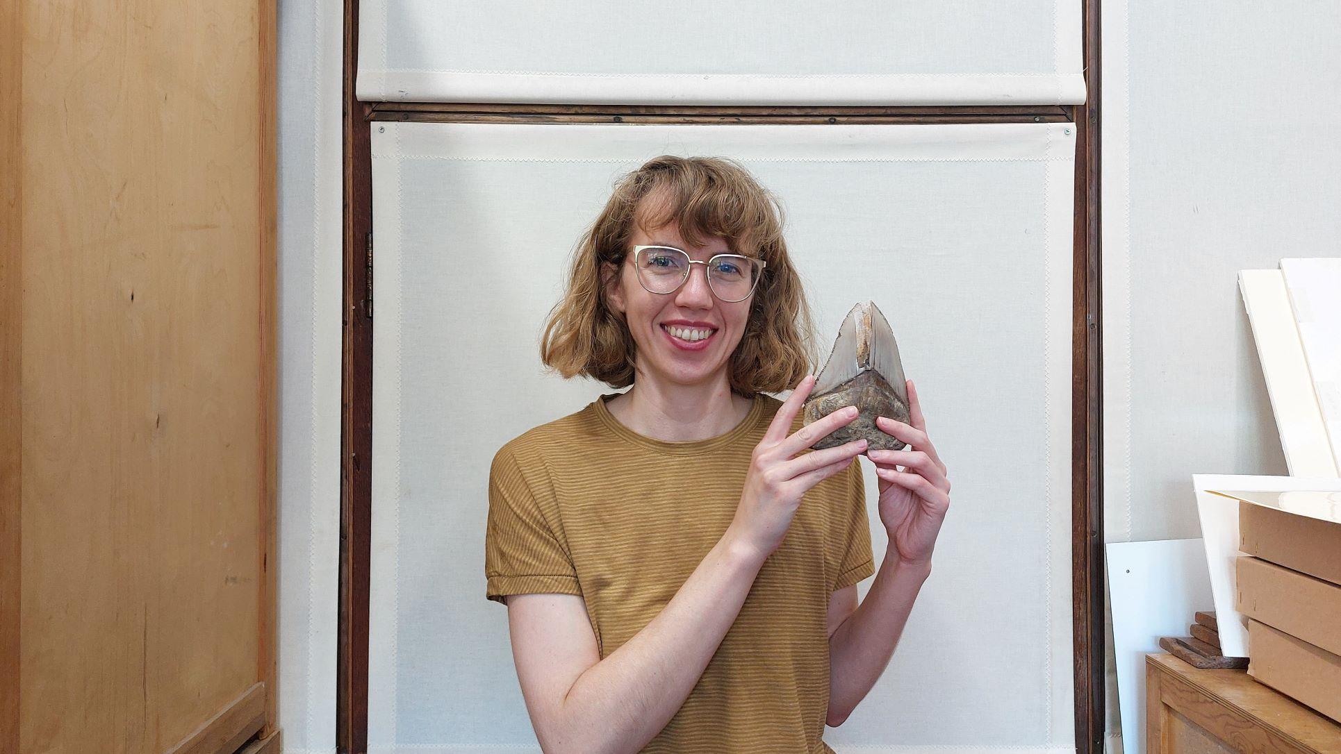 Photo of woman smiling holding giant shark tooth