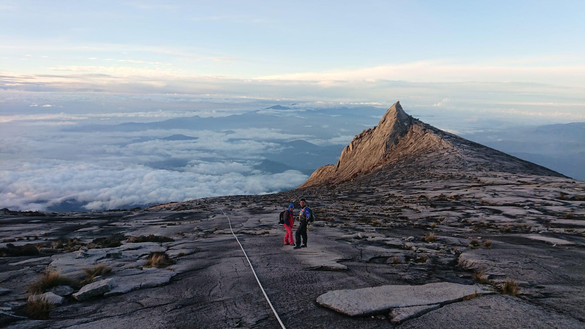Photo of a sharp mountain peak with two people standing on the flanks