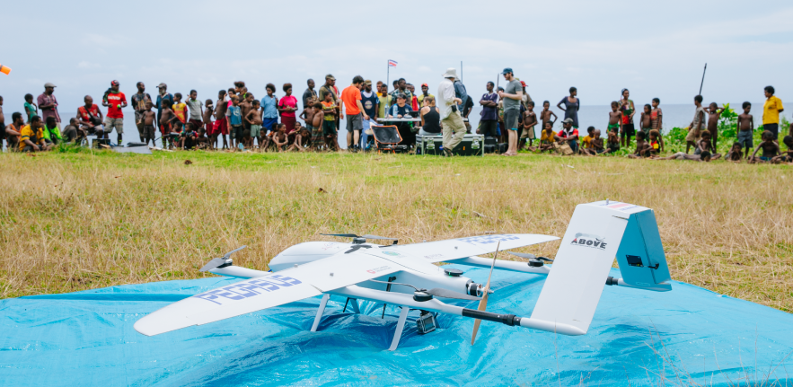 Drone ready to launch in the foreground with research scientists and Manam islanders gathered in the background; image credit Mathew Wordell