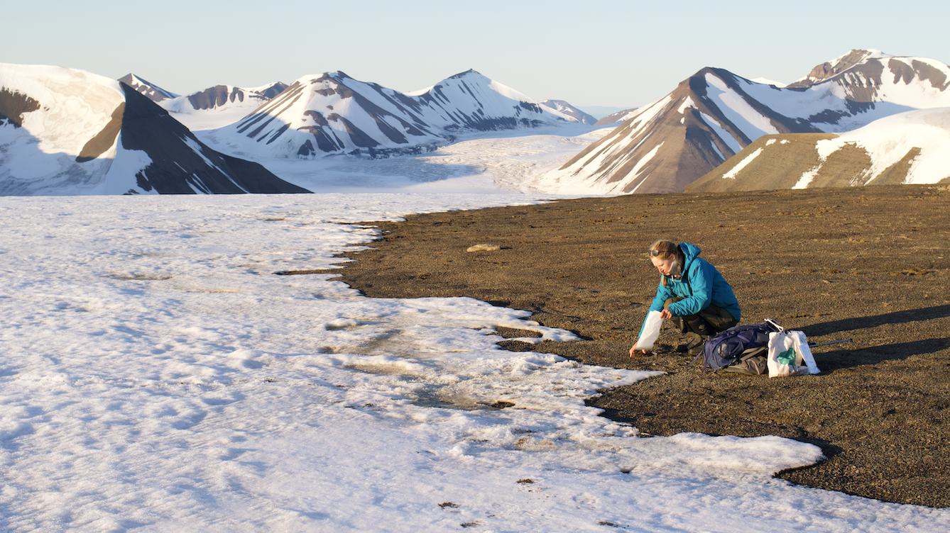 Photo showing a woman knelt down at the edge of some ice taking a sample